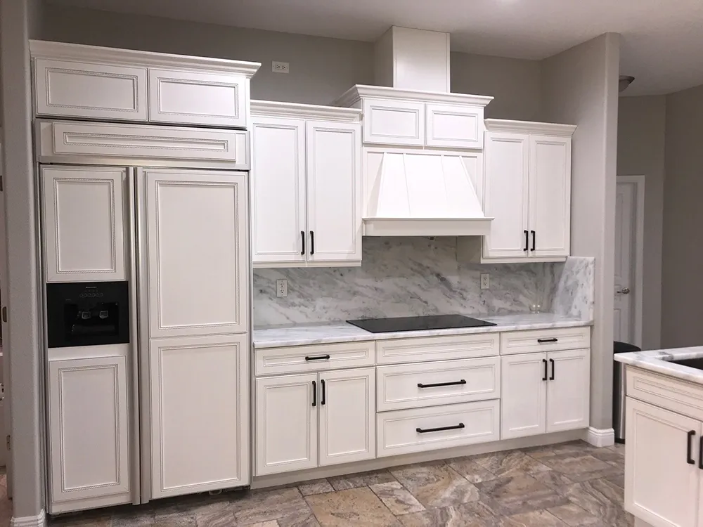 The same Sarasota kitchen after painting, with white cabinets, a white hood, marble backsplash and black hardware