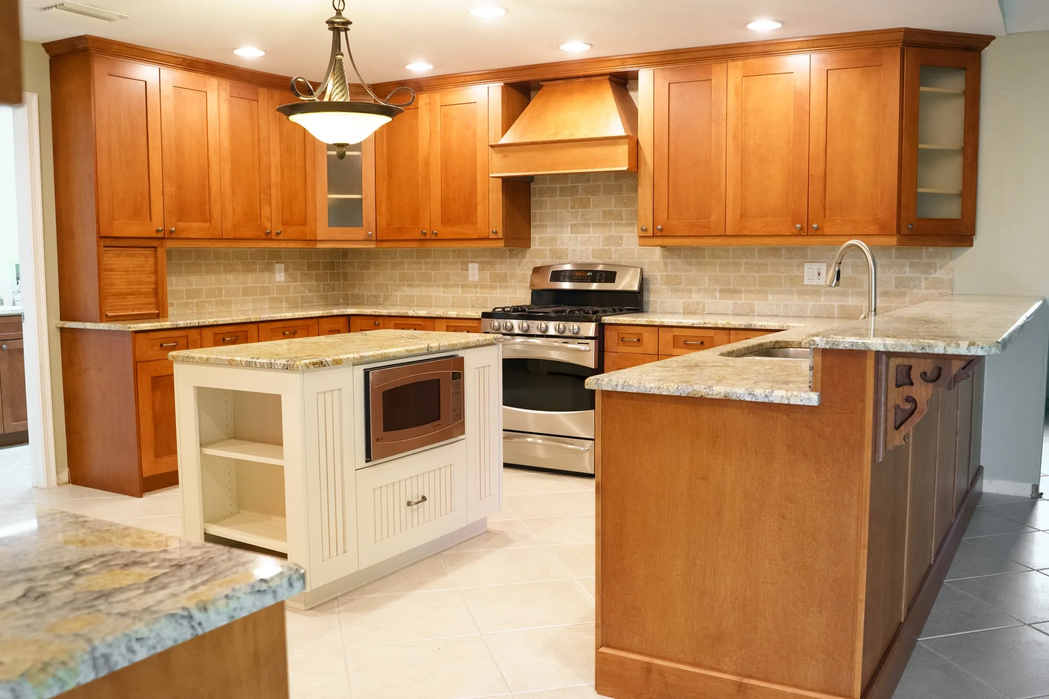 Tampa kitchen before painting, with honey maple shaker cabinets, a contrasting cream island, stone backsplash and granite counters